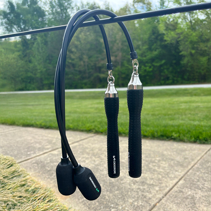 Ropeless One Black (Ropeless) jump ropes with silver connections hanging on a metal rod outdoors.