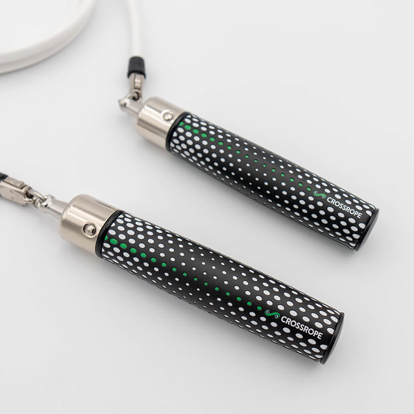 Power Starter Jump Rope Set A close-up of a jump rope with two black Power Handles covered in white polka dots, featuring a green dotted center stripe, silver metal caps, connected to a white 1/2 LB jump rope. The brand name 'CROSSROPE' is printed in white on the handles