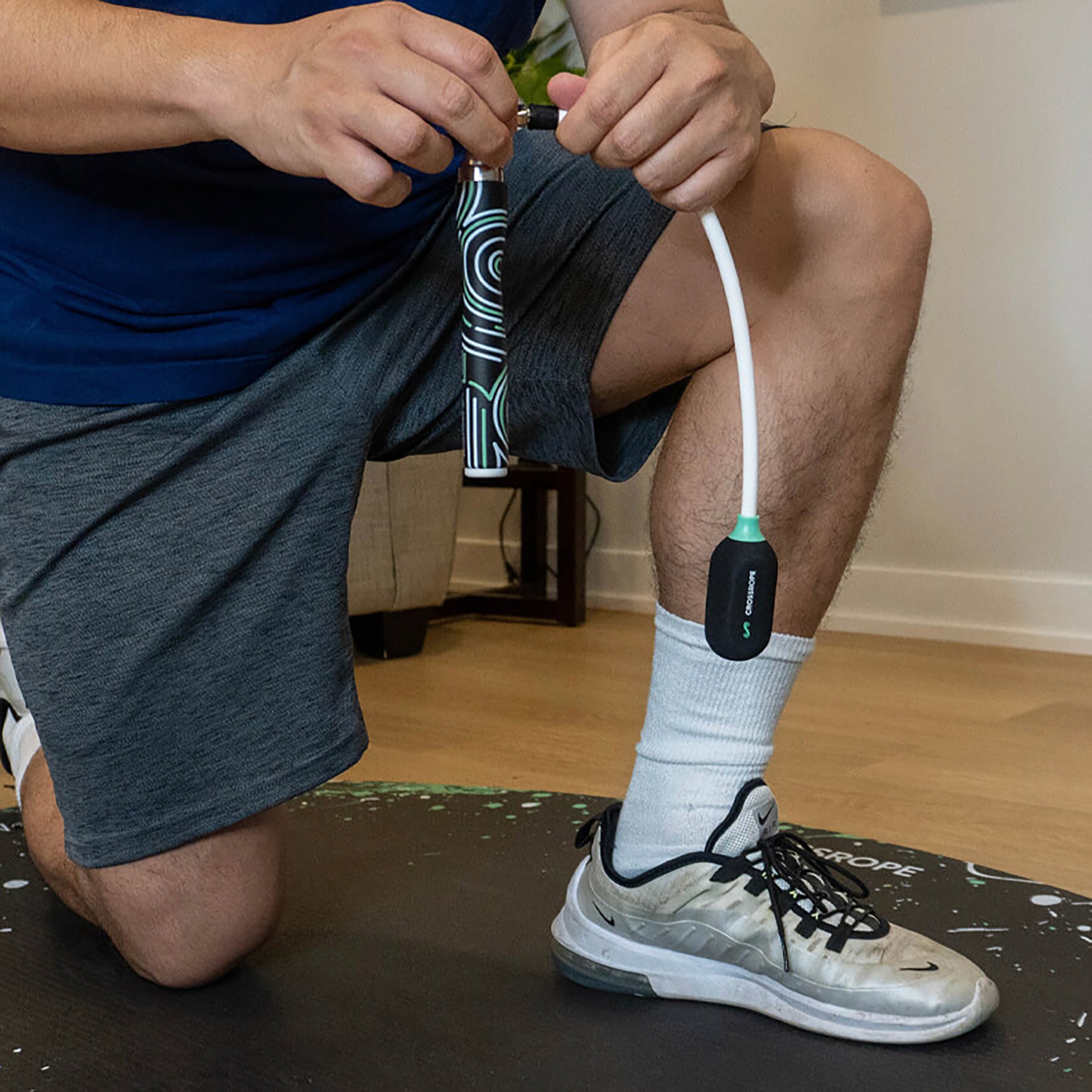 Ropeless Get Lean Set Person connecting Ropeless to a Slim Handles while kneeling on a jump rope mat on a wooden floor.