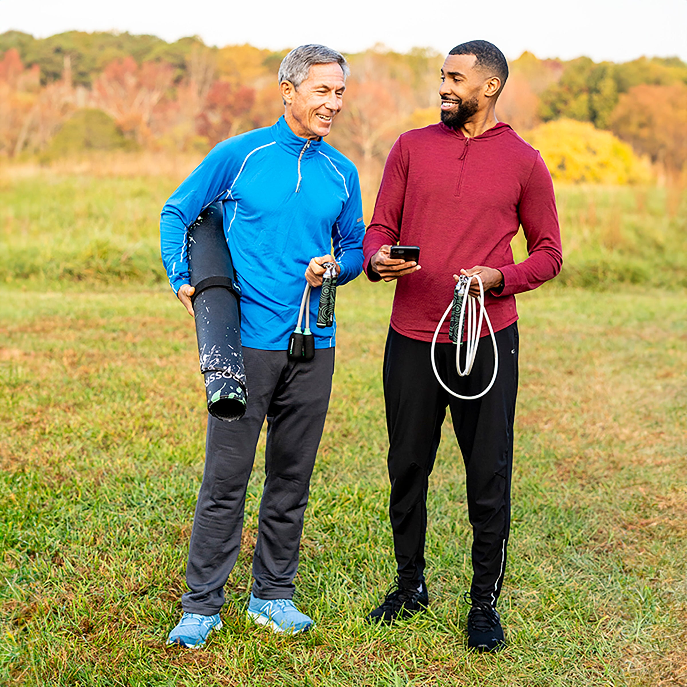 Jump Rope Mat (Splash) Two men standing in a grassy field with trees in the background, holding Crossrope jump rope gear.